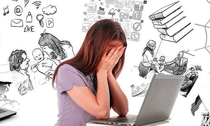 Mulher diante de um notebook cobrindo o rosto com as mãos, cercada por ilustrações relacionadas a trabalho, comunicação e vida digital.