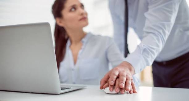 Mulher demonstra desconforto enquanto um homem coloca a mão sobre a dela diante de um notebook.
