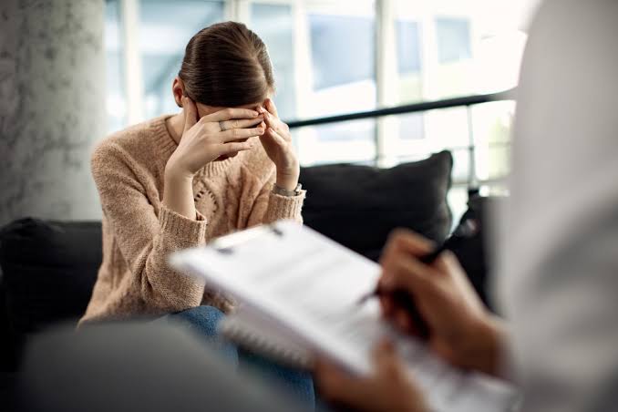 Mulher cobre o rosto durante uma sessão de psicoterapia enquanto o profissional faz anotações.