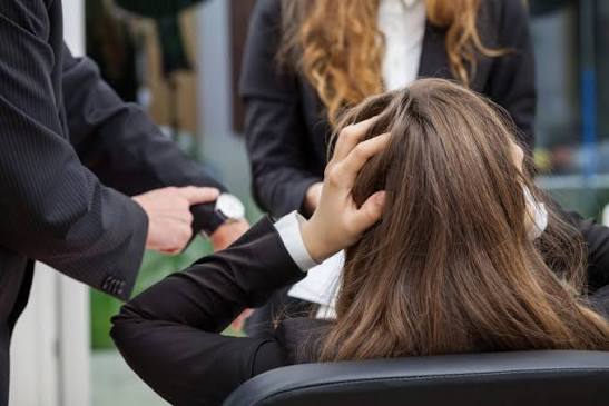 Mulher sentada segura a cabeça enquanto um homem aponta para o relógio em um ambiente de trabalho.