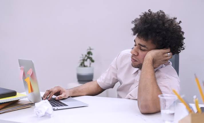 Mulher sentada diante de um notebook, apoiando a cabeça na mão e demonstrando cansaço durante a atividade profissional.
